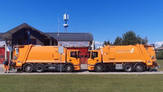 Deux camions poubelles orange sont garés l'un à côté de l'autre devant un bâtiment.