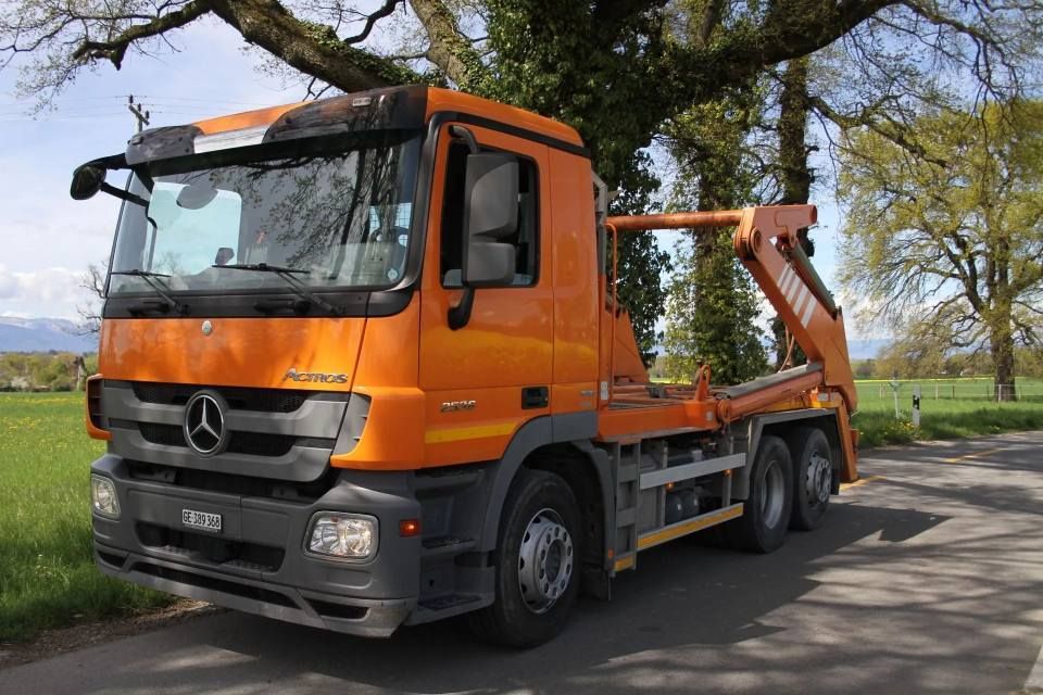 Un camion-benne orange est garé sur le bord d'une route.