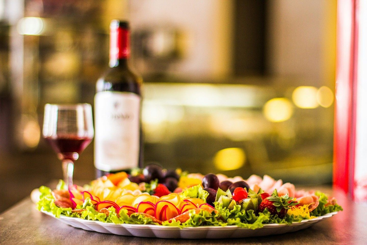 Una botella y una copa de vino junto a una colorida ensalada en la mesa de un restaurante.