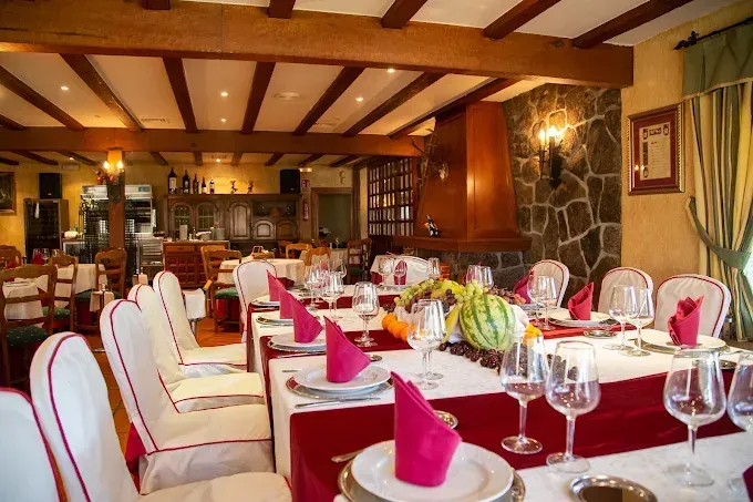 Comedor de restaurante con mesas preparadas para comer, incluidas sillas blancas, manteles rojos y una chimenea de piedra.