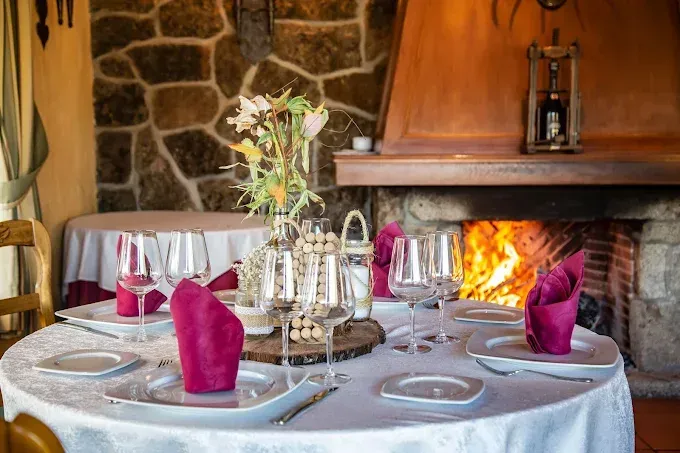 Mesa puesta para cenar en un restaurante rústico, con chimenea al fondo.