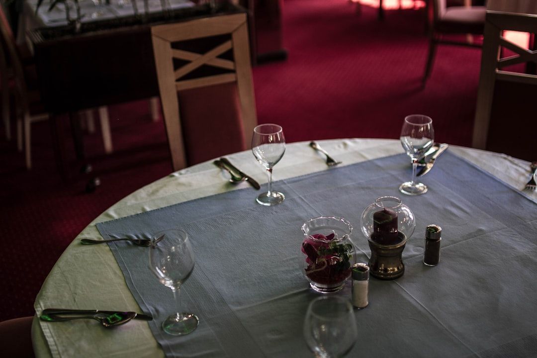 Mesa de comedor vacía con vasos, cubiertos y condimentos en un restaurante con poca luz.