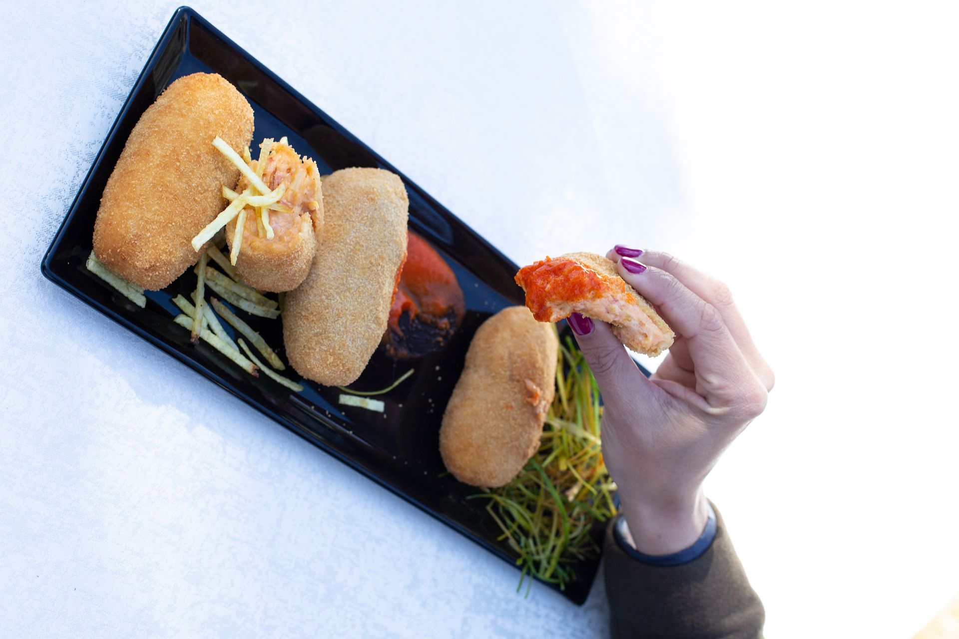 Persona que sostiene un alimento empanizado que revela un relleno rojo, en un plato con otros alimentos similares.