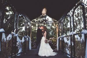 Pareja besándose bajo un cenador ornamentado con cintas blancas y flores.