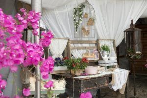 Flores rosas enmarcan una disposición rústica: cajas de madera, fondo drapeado en blanco, jaula de pájaros y elementos decorativos.