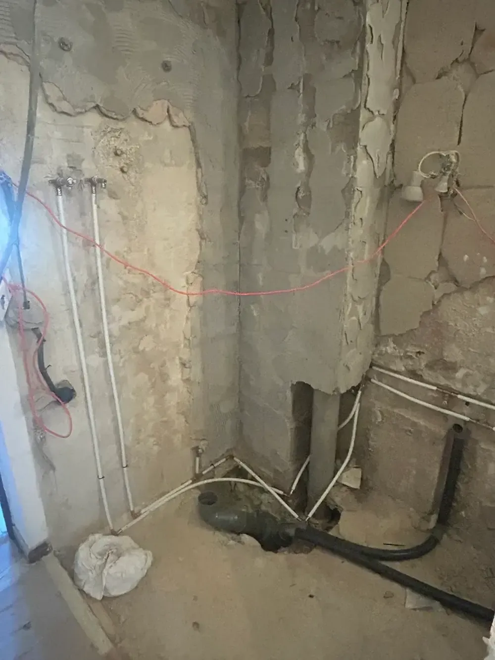 Pared interior en proceso de renovación; tuberías y cableado expuestos visibles.