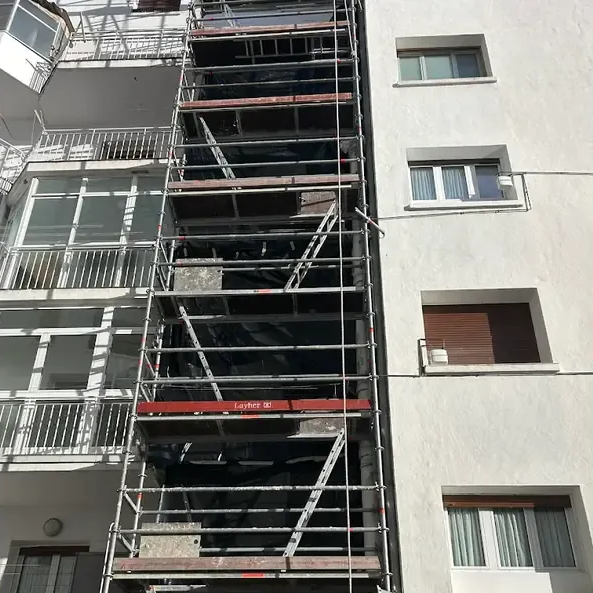 Andamios en la fachada blanca de un edificio, posiblemente para reformas. Contiene ventanas y balcones.