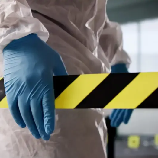 Persona con traje de materiales peligrosos sosteniendo cinta de precaución amarilla y negra.