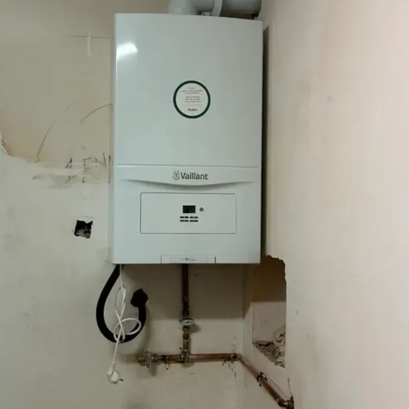 Caldera Vaillant blanca montada en una pared dañada con tuberías de cobre debajo.