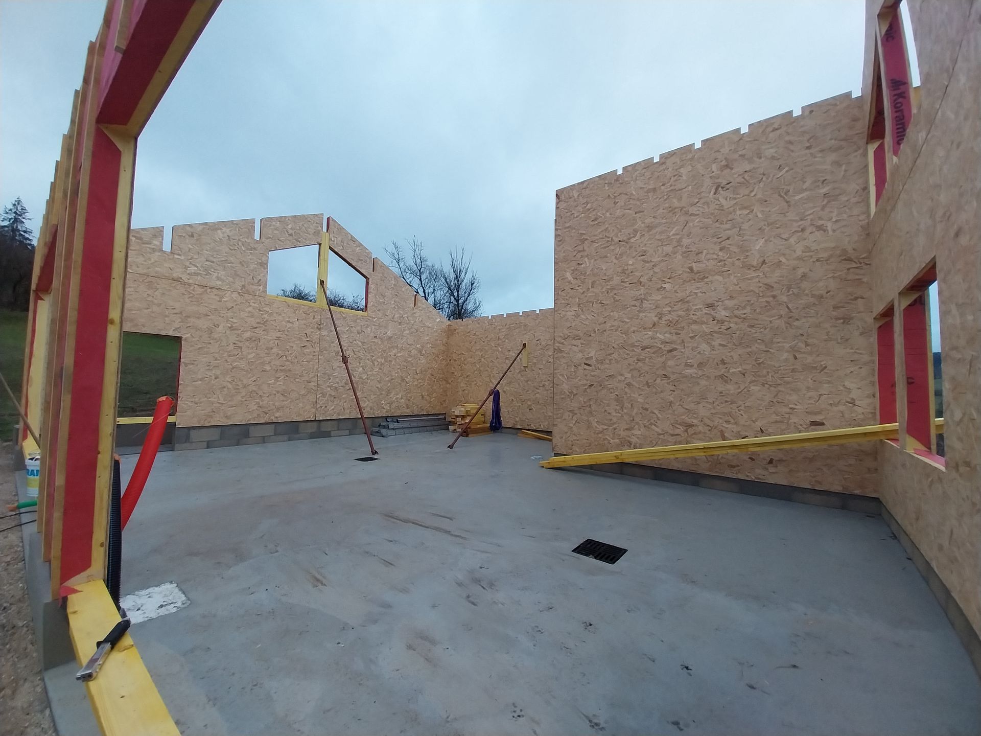 Vue intérieure d'un bâtiment en construction, avec des murs en bois et un sol en béton.
