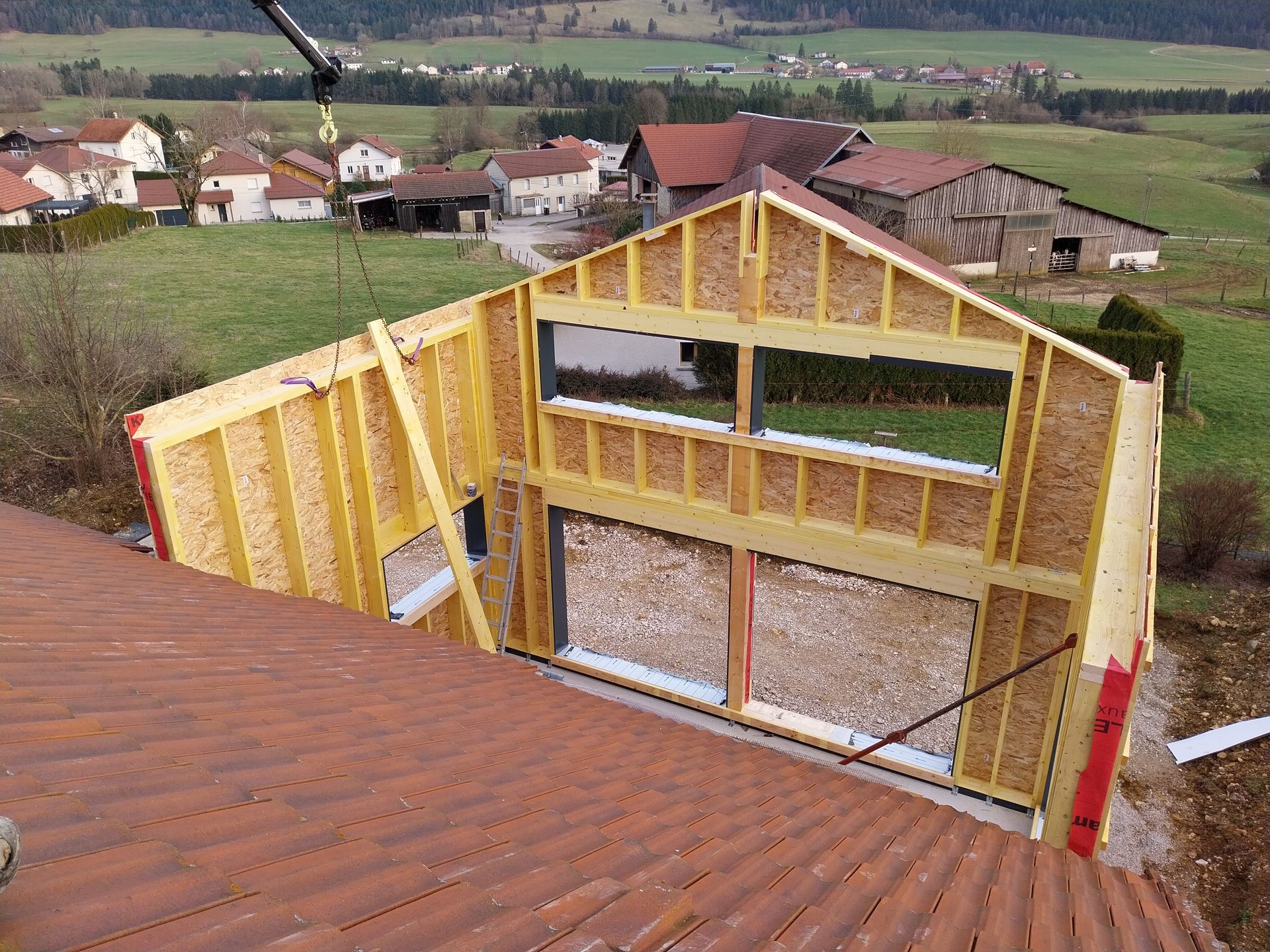 Construction d'une ossature bois, grue soulevant une section de mur, cadre rural.