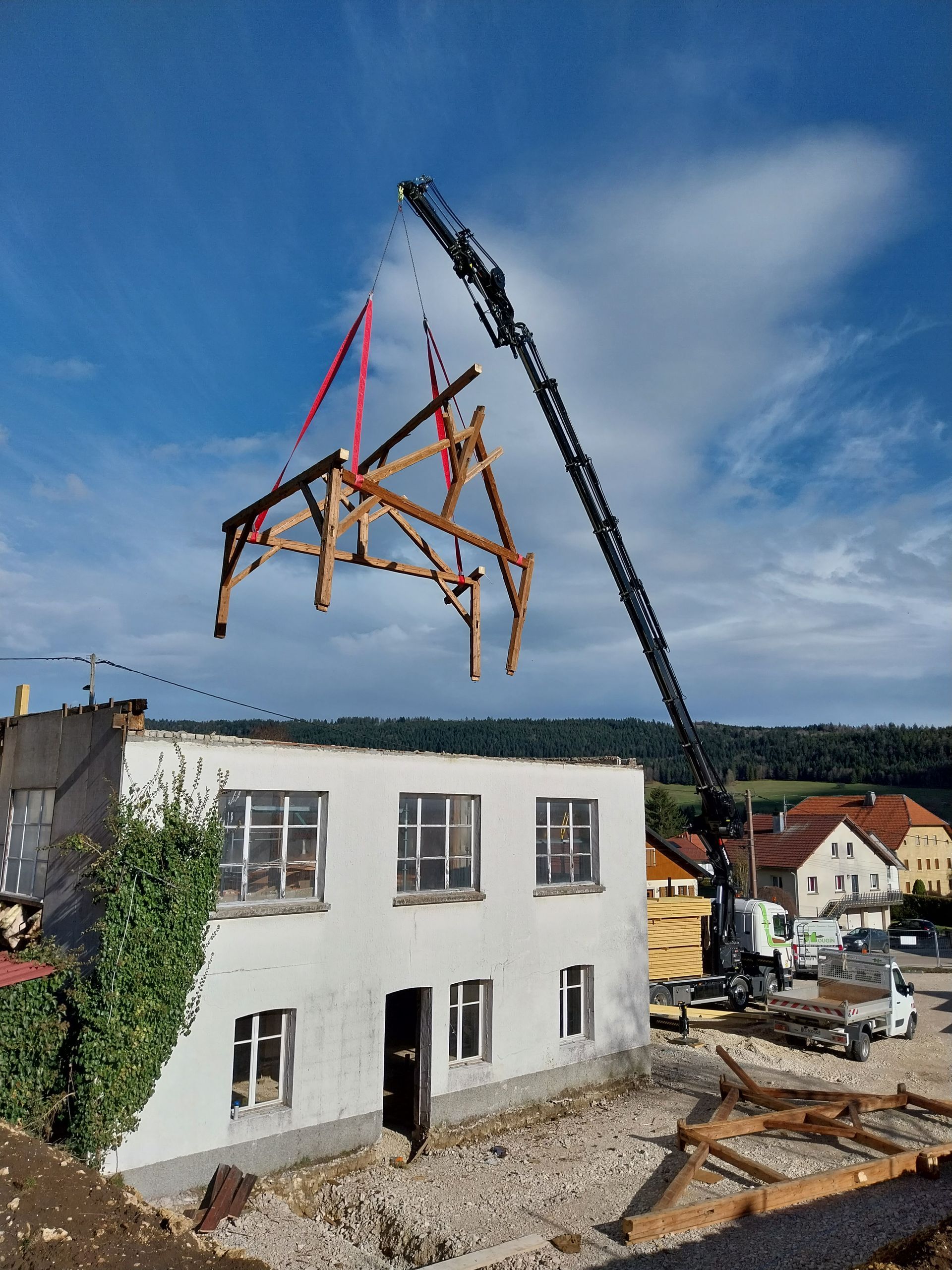 Une grue soulève une charpente en bois d'un bâtiment blanc vitré. Scène de démolition par une journée ensoleillée.