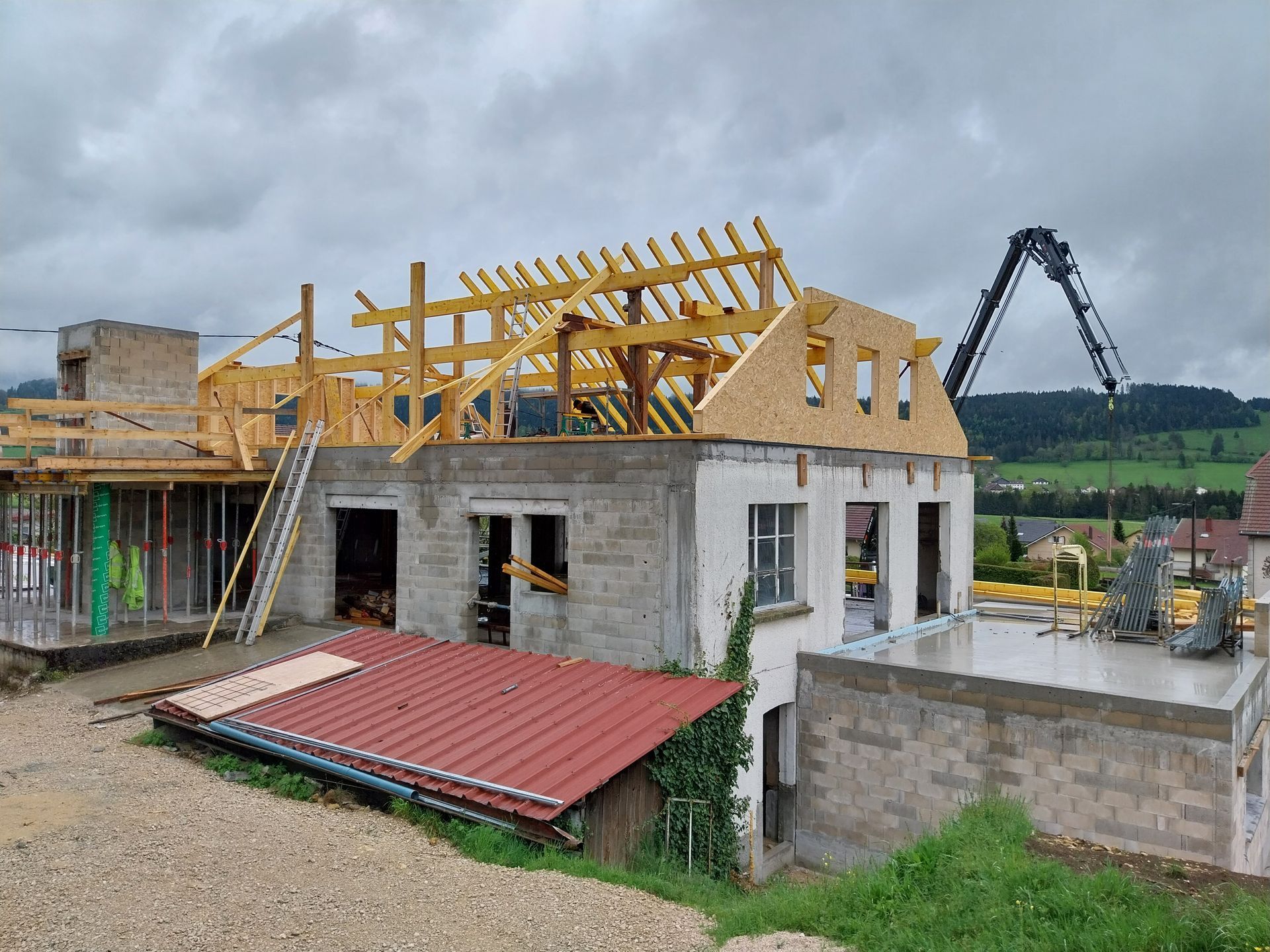 Construction d'une maison à charpente apparente. Grue et ciel couvert.