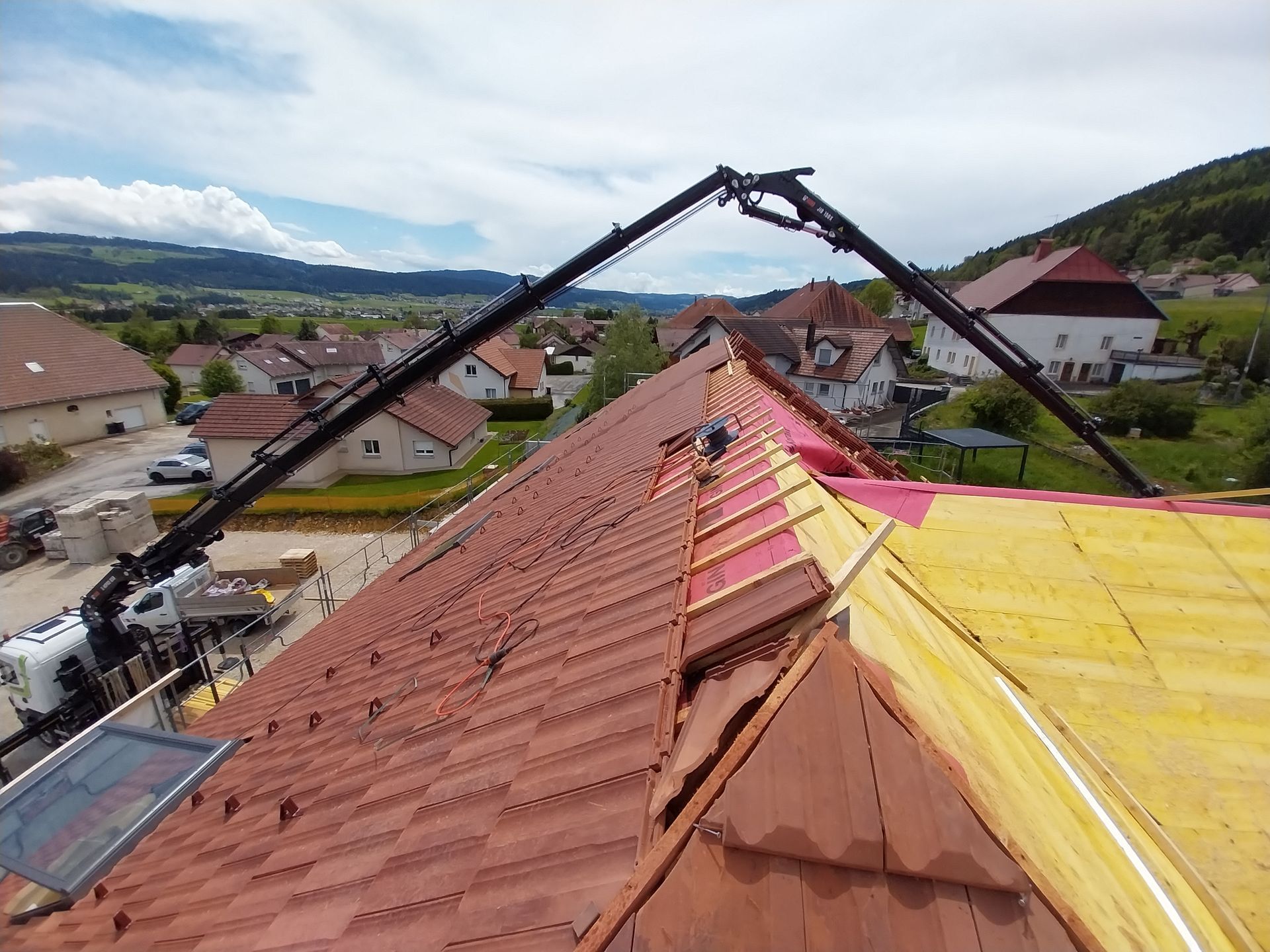 Un toit en cours de réparation à l'aide de deux bras articulés, dans un cadre rural.