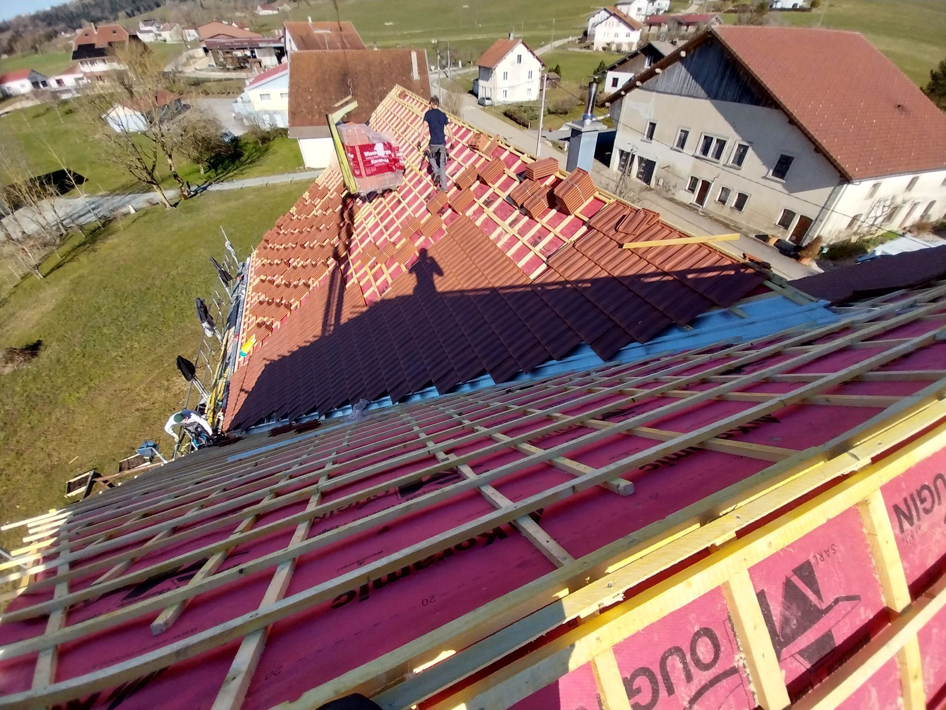 Des ouvriers du bâtiment remplacent un toit de tuiles rouges sur un bâtiment en milieu rural.