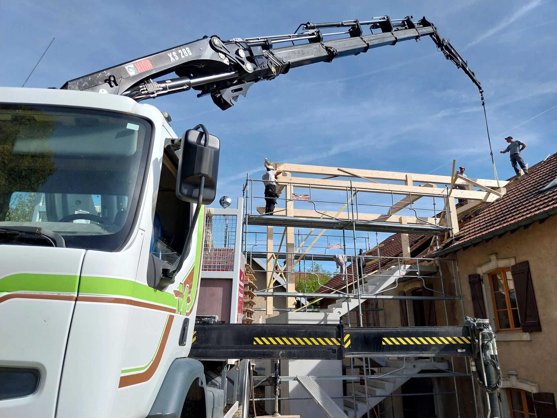 Camion-grue déversant du béton sur une charpente de toit avec un ouvrier ; journée ensoleillée.