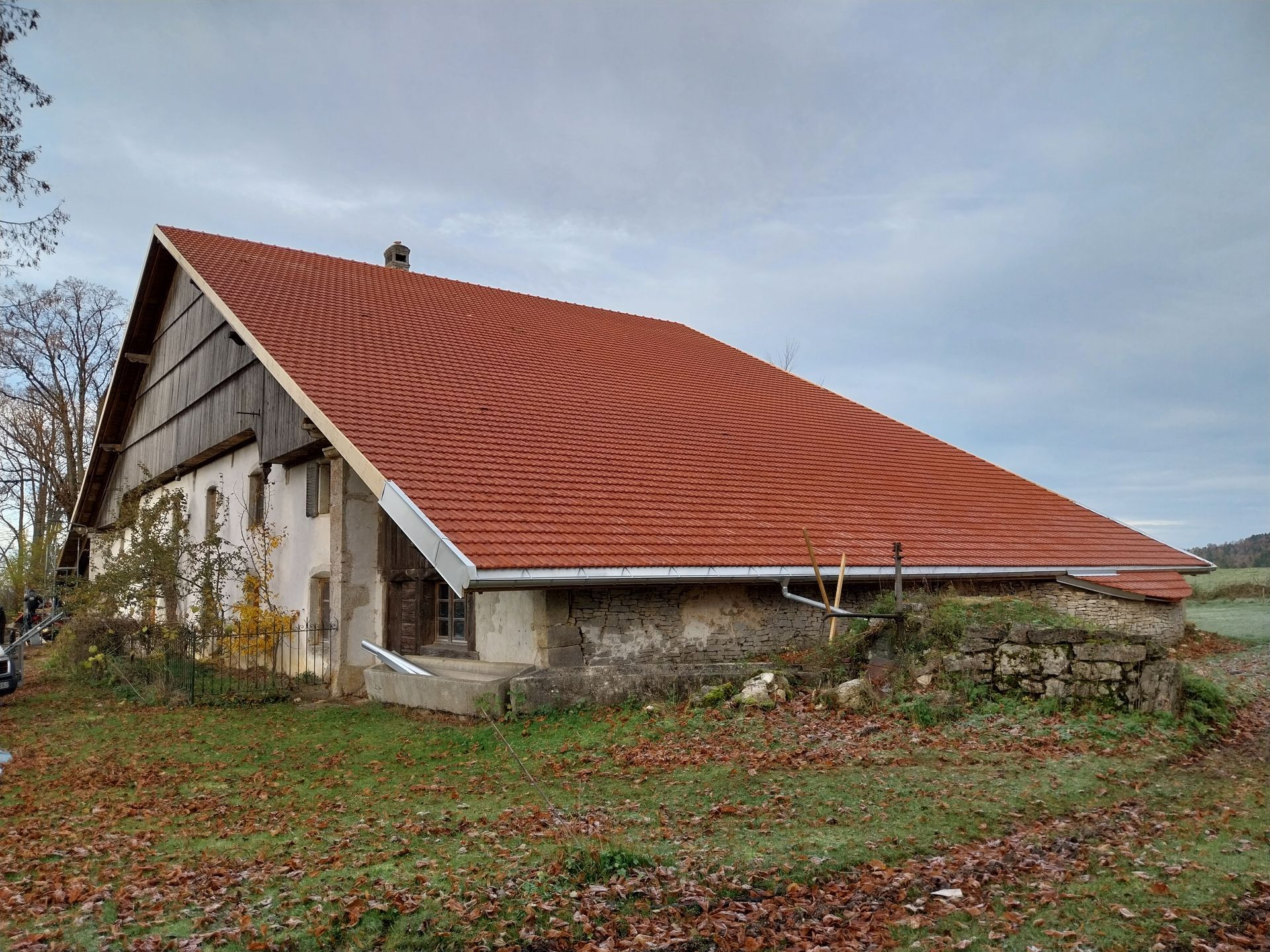 Vieux bâtiment en pierre avec un grand toit de tuiles rouges sous un ciel nuageux.