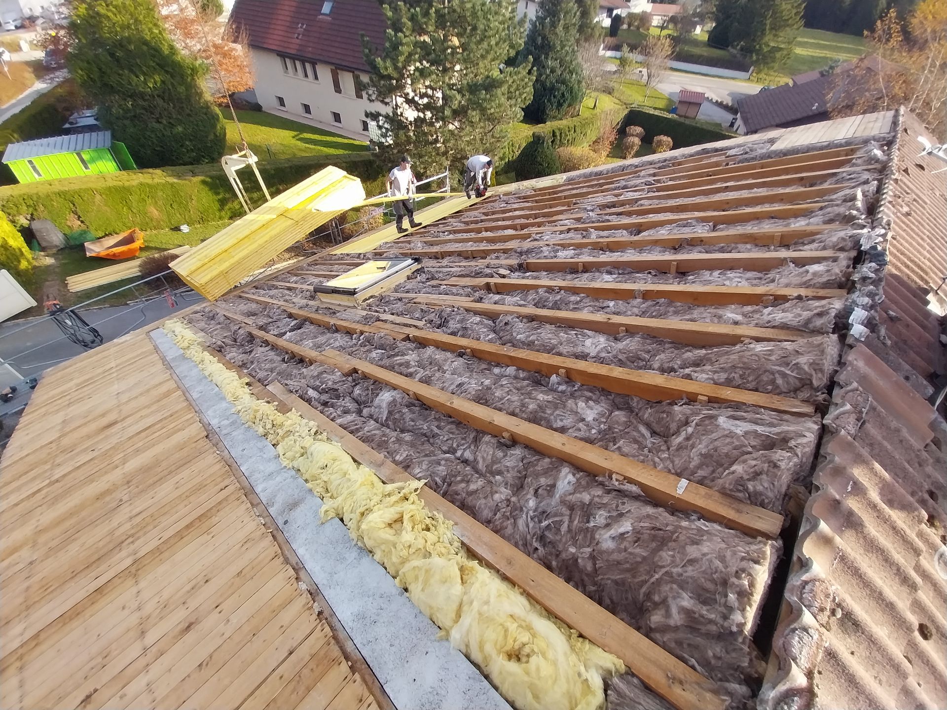 Installation d'isolant de toiture sur une maison : ouvriers, poutres en bois, isolant et tuiles.