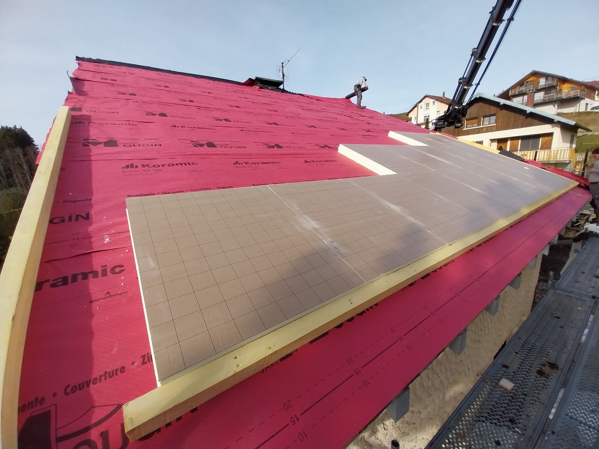 Toiture avec sous-couche rose, isolation et panneaux solaires. Charpente en bois apparente.