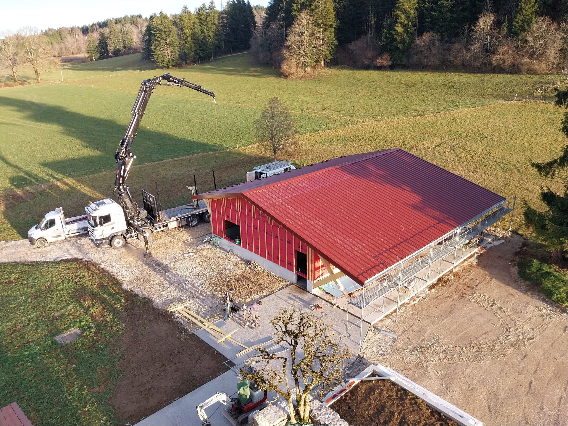 Un bâtiment au toit rouge en construction ; un camion-grue à côté, sur un terrain herbeux.