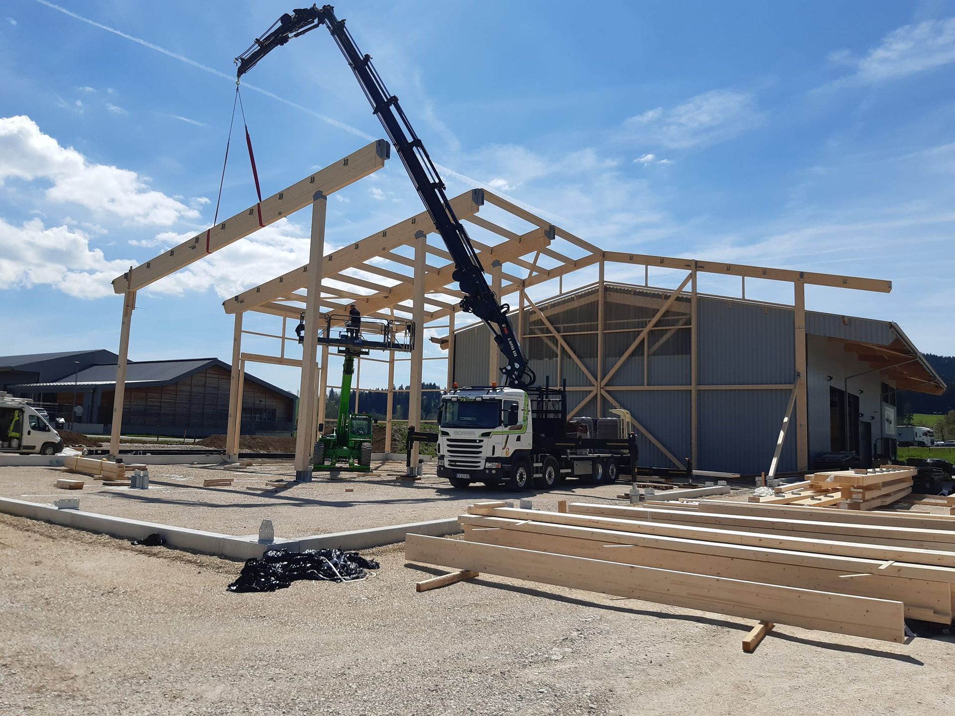 Chantier de construction, une grue soulève une poutre en bois pour la poser sur un bâtiment en construction.