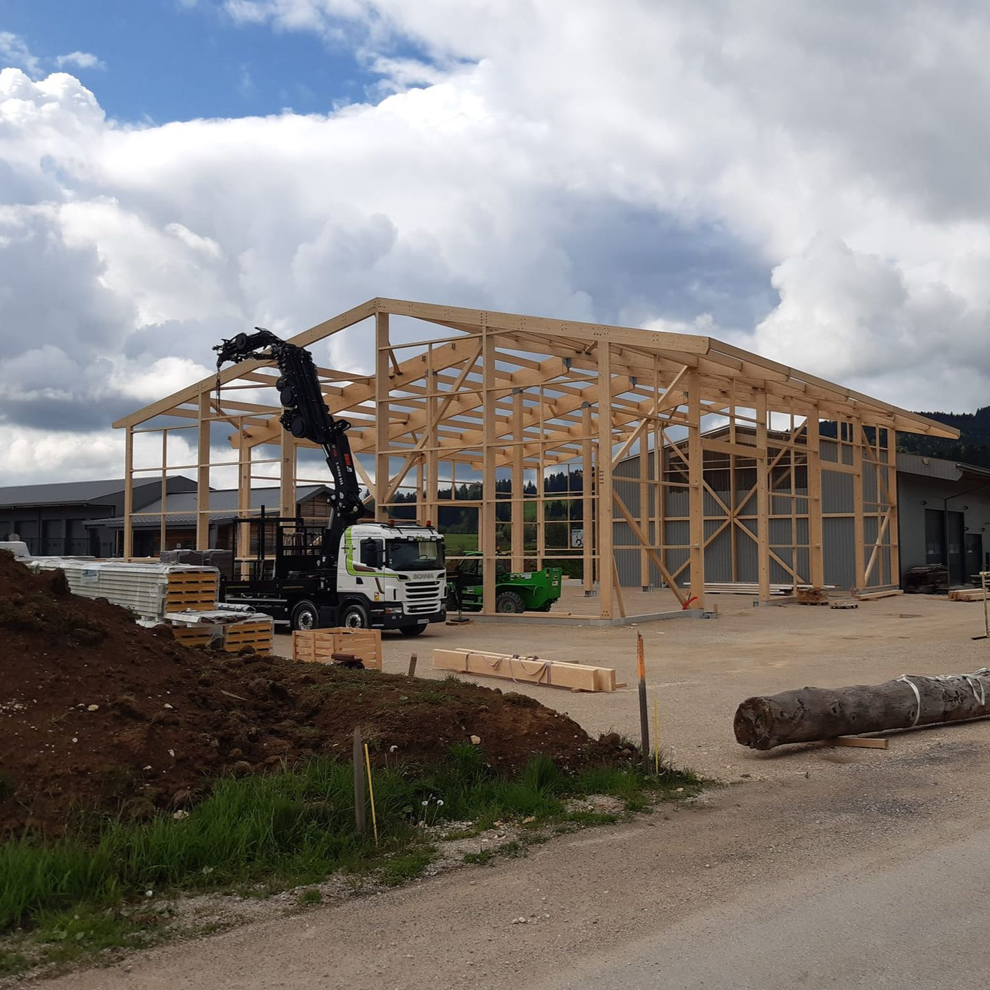 Structure en bois d'un bâtiment en construction, grue soulevant des poutres, ciel nuageux.