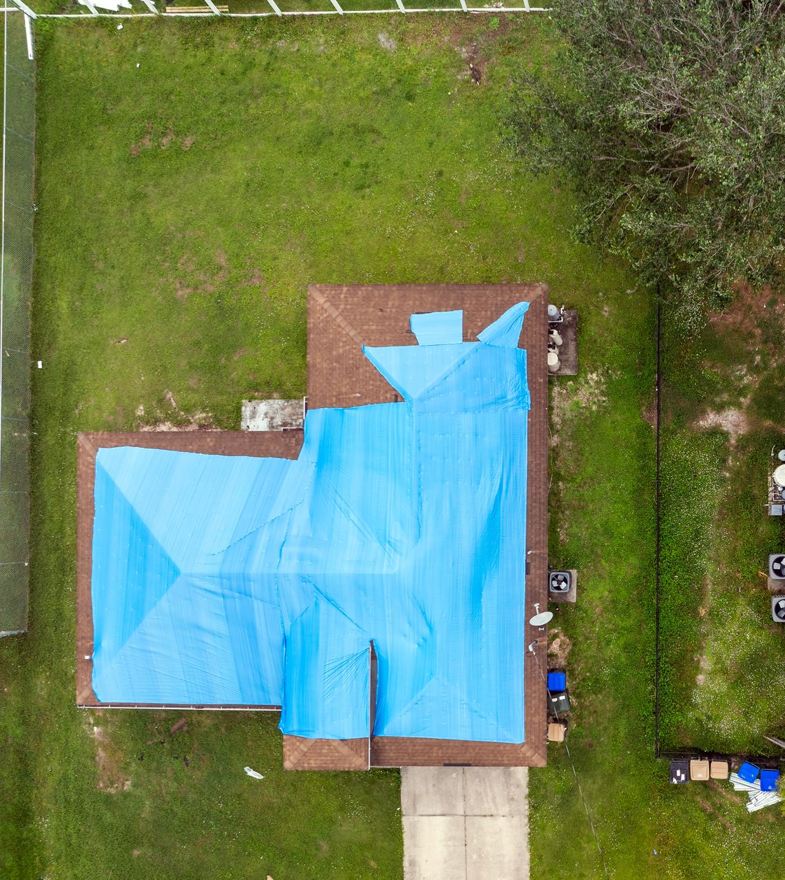 Vue aérienne d'une maison dont une partie du toit est recouverte d'une bâche bleue ; elle est entourée d'herbe verte.