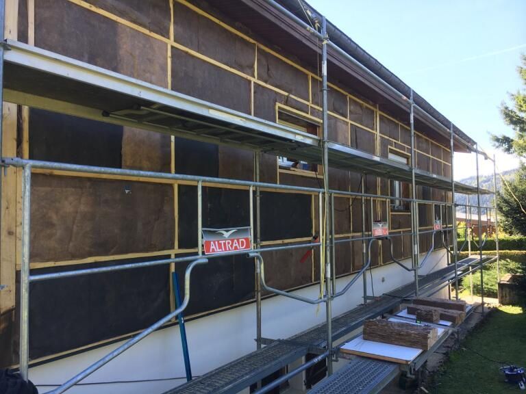 Échafaudages autour d'une maison avec isolation et poutres en bois installées sur le mur extérieur.