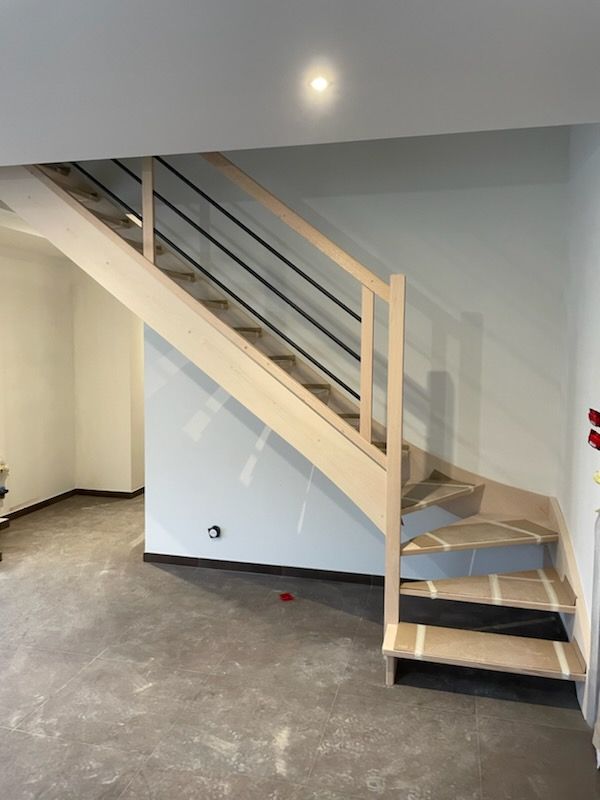 Escalier en bois clair avec rampes en métal noir sur des murs bleus et blancs.