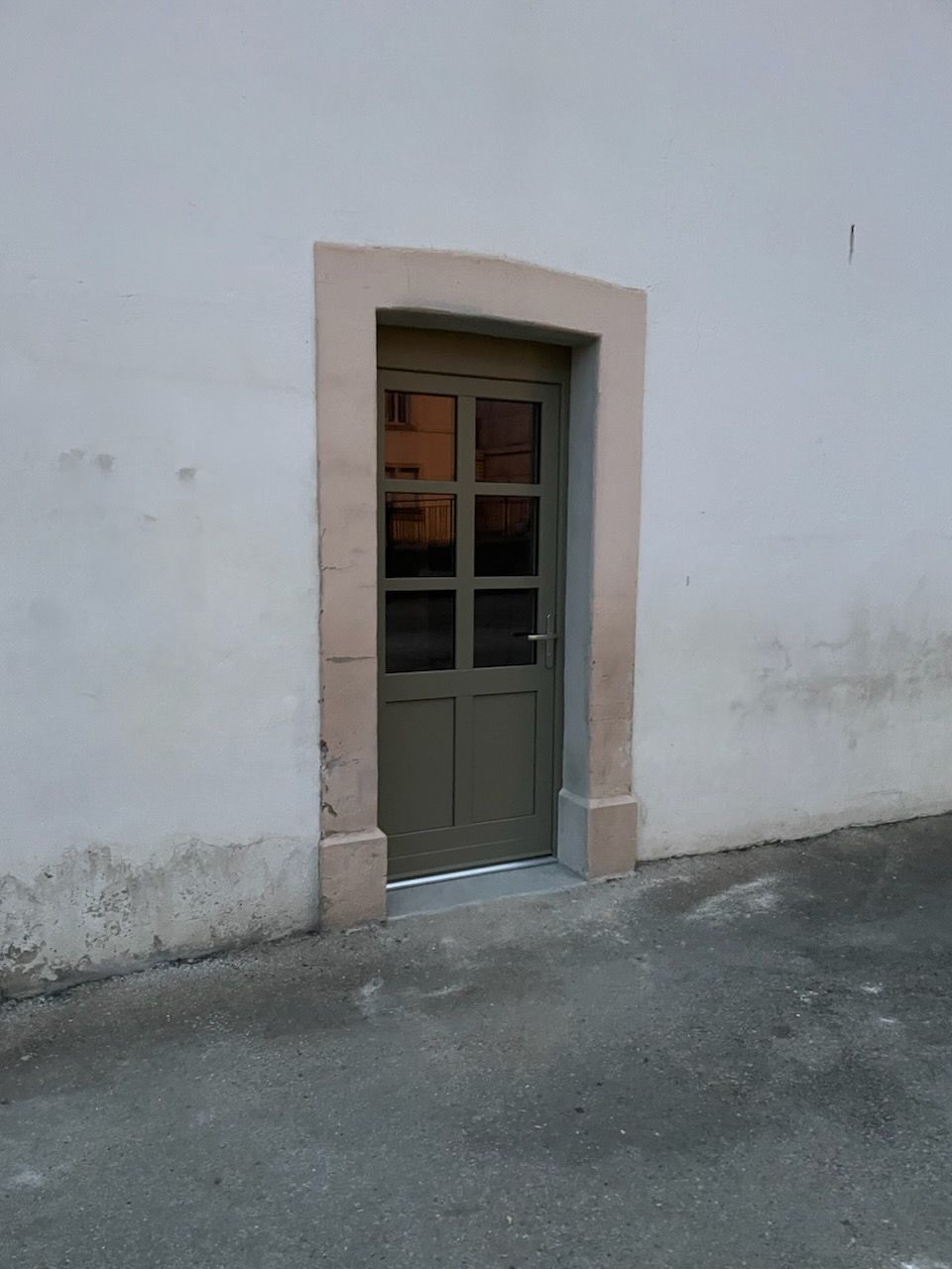 Porte verte dans un mur blanc avec un encadrement en pierre.