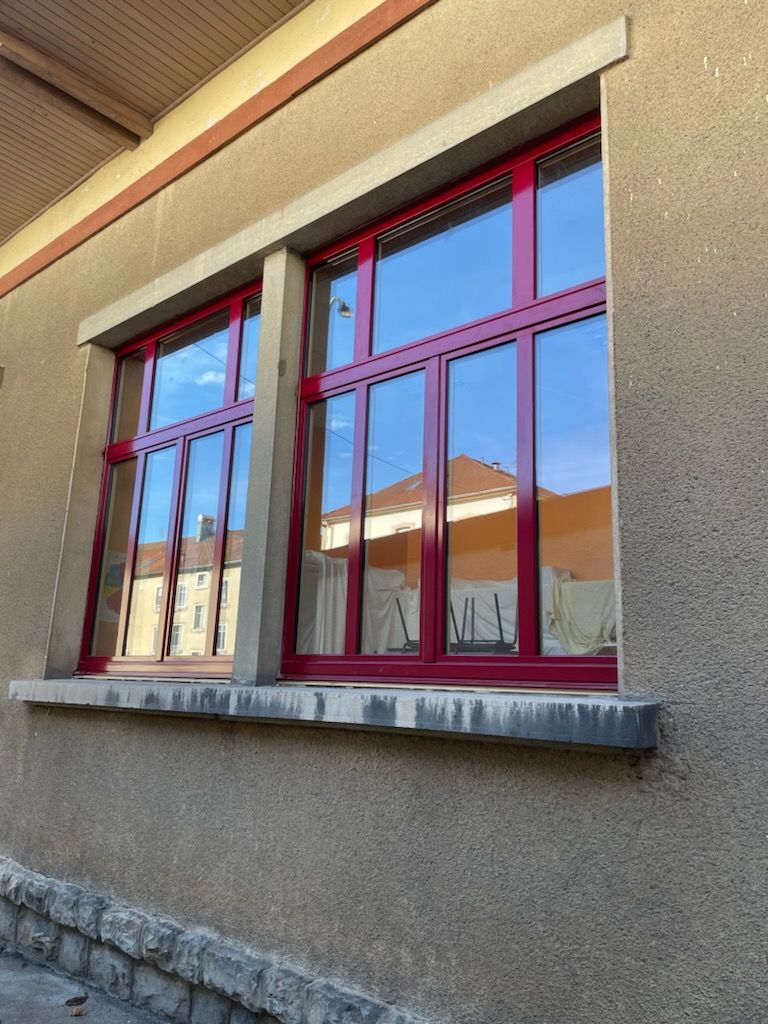 Fenêtre à cadre rouge reflétant les bâtiments. Façade beige du bâtiment.