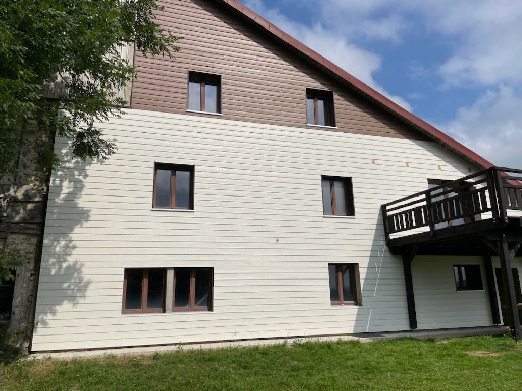 Immeuble de plusieurs étages, beige et marron, avec de nombreuses fenêtres et un petit balcon, situé sur une colline herbeuse.