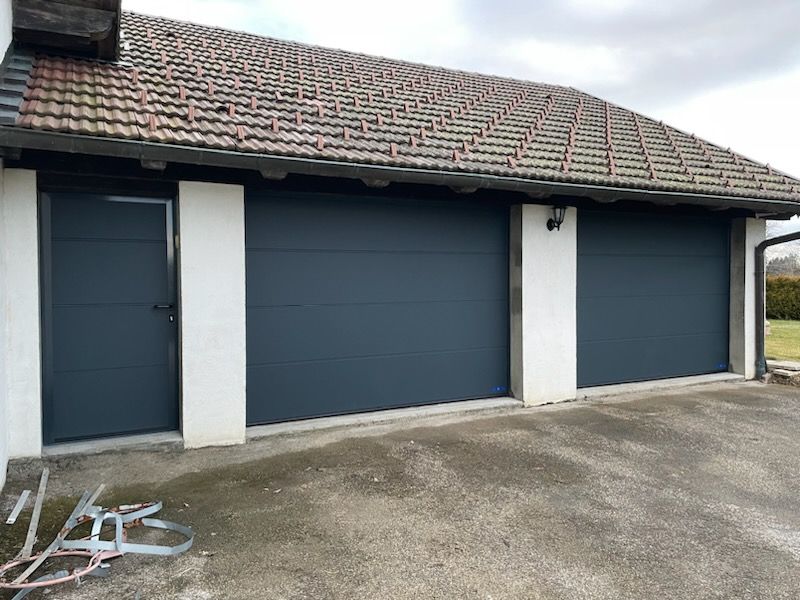 Portes de garage gris foncé avec une porte latérale assortie sur un bâtiment au toit de tuiles.