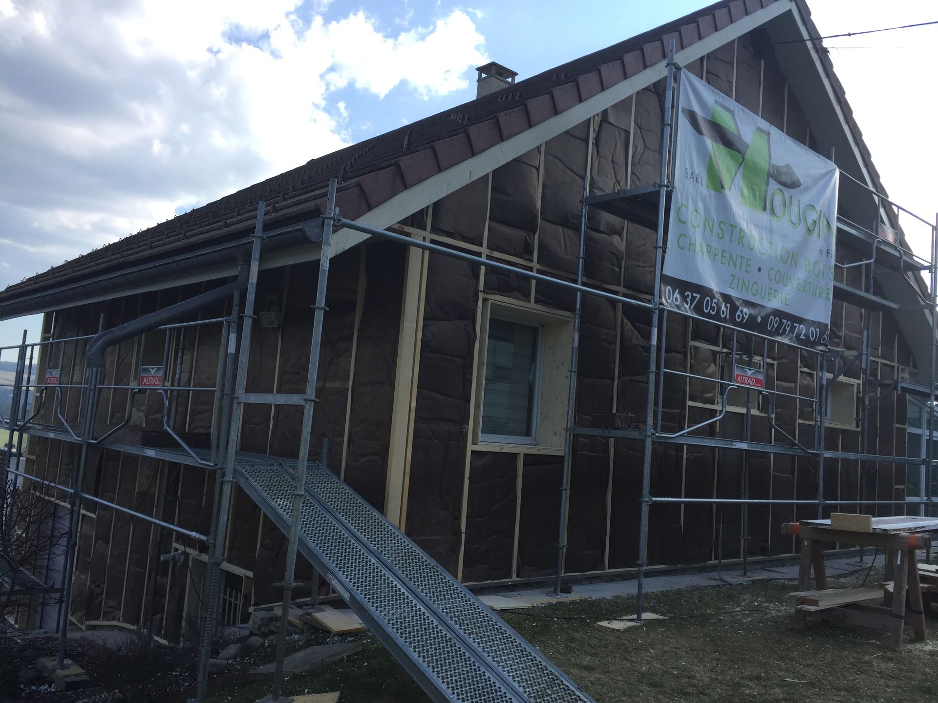 Façade de la maison en construction, avec échafaudages, isolation et banderole.