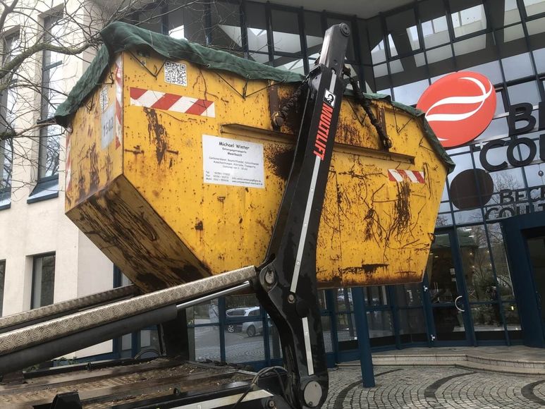 Vor einem Gebäude steht ein gelber Müllcontainer.