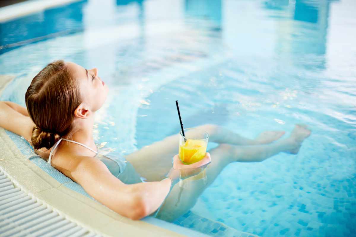 A woman is laying in a swimming pool holding a drink.
