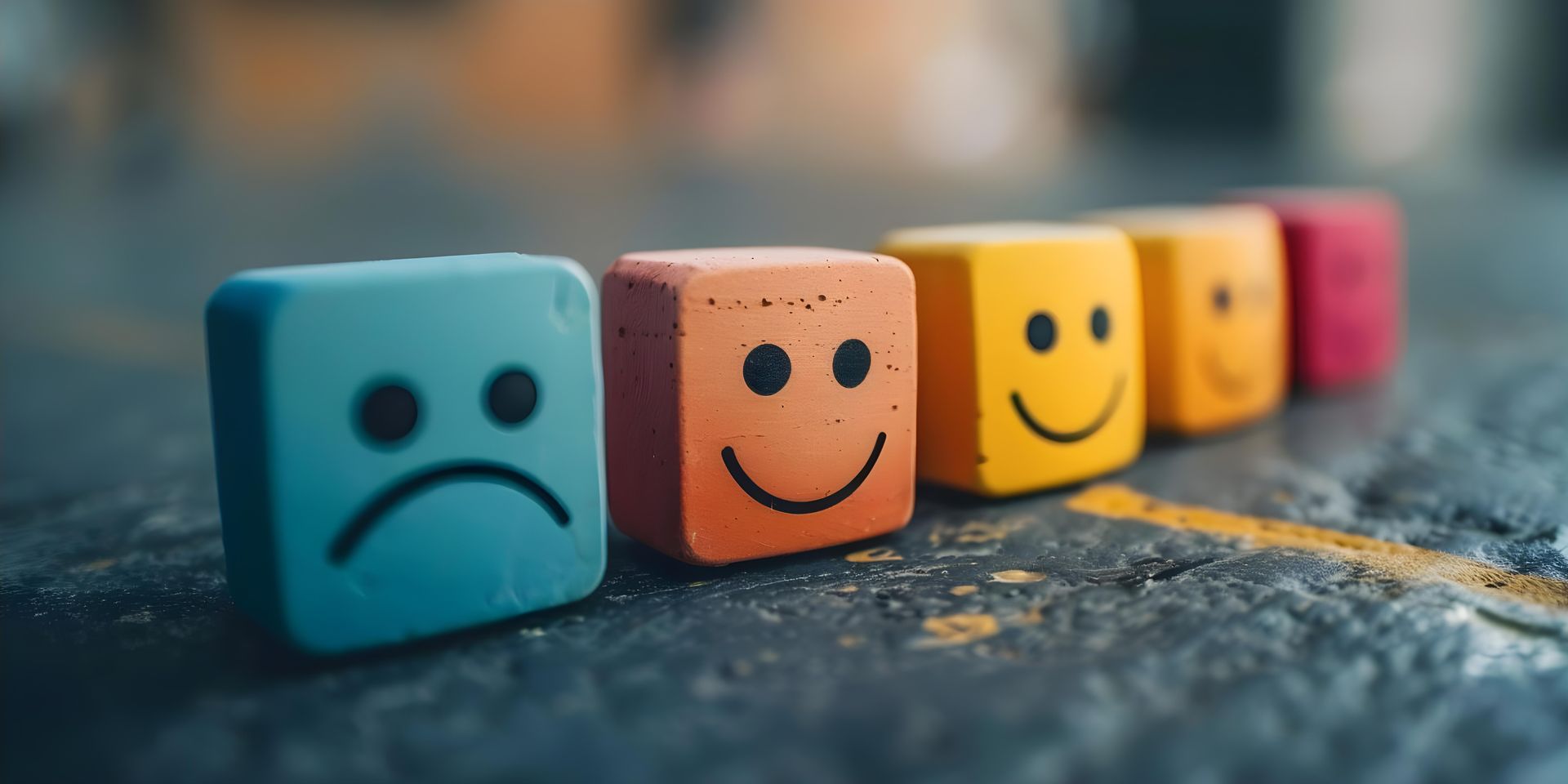 Rangée de blocs colorés ornés d'émoticônes, allant de la tristesse à la joie, sur un fond sombre.