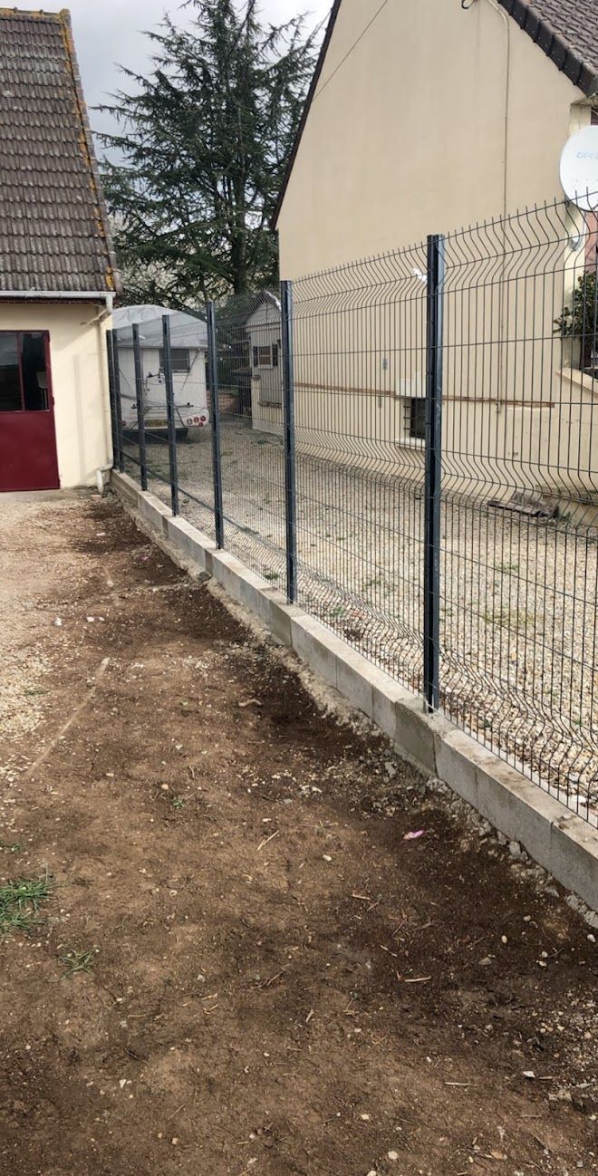 Une nouvelle clôture métallique longeant la limite de propriété, installée sur une base en béton.