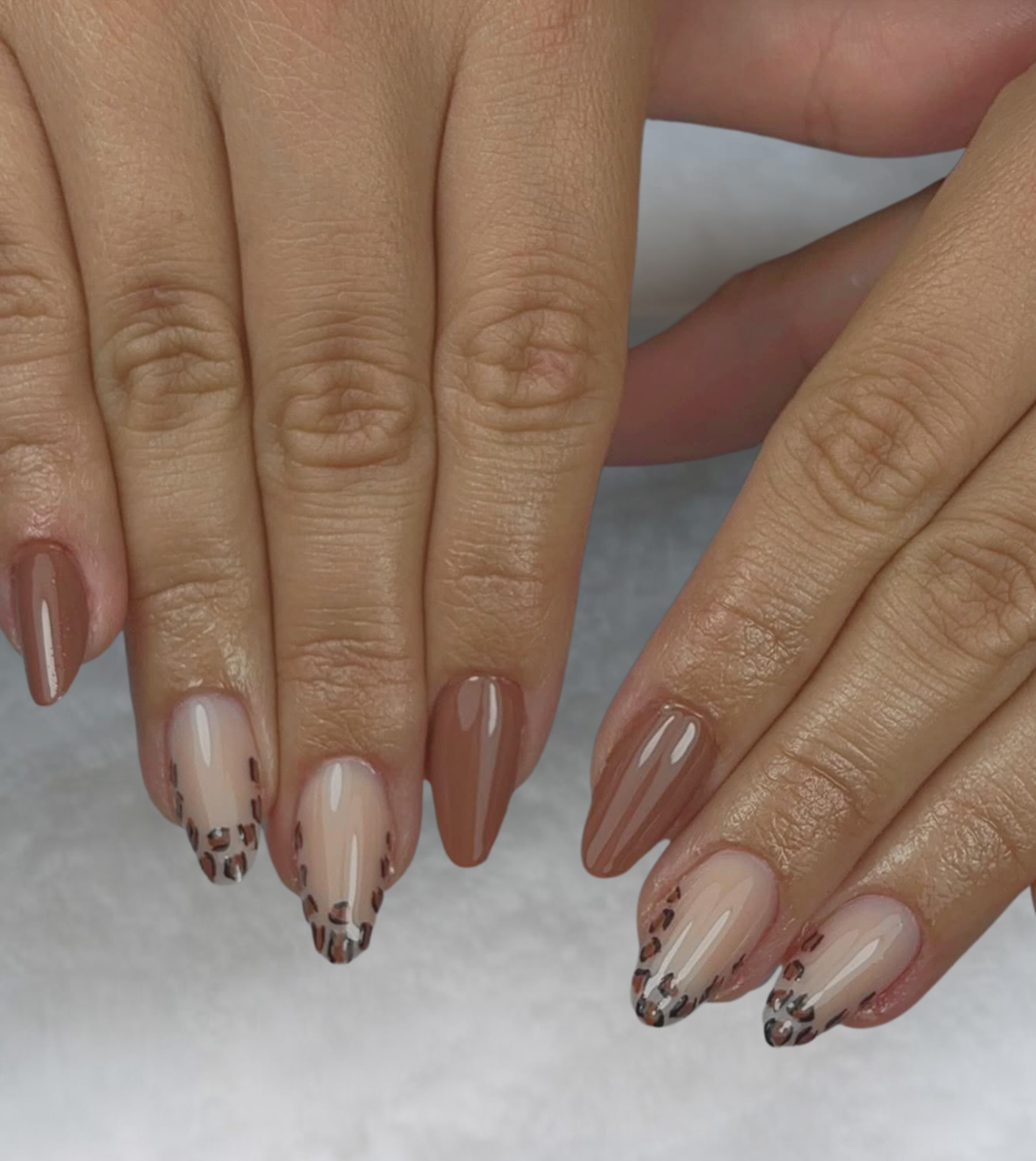 Main aux ongles carrés roses, dont un pailleté, posés sur une surface blanche et moelleuse.