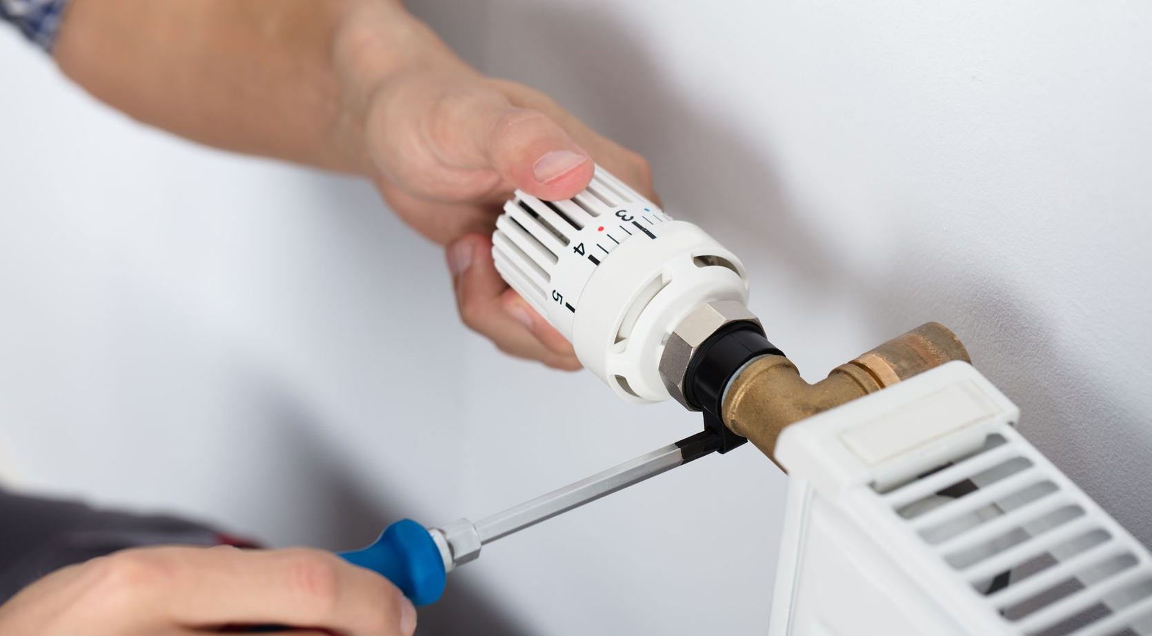 Mains ajustant une vanne de radiateur avec un tournevis et une clé lors d'une réparation