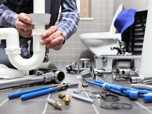 Un plombier assemble un tuyau d'évacuation blanc, ses outils éparpillés sur le comptoir d'une salle de bain.
