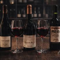 Trois bouteilles de vin rouge et deux verres remplis, posés sur un comptoir sombre.