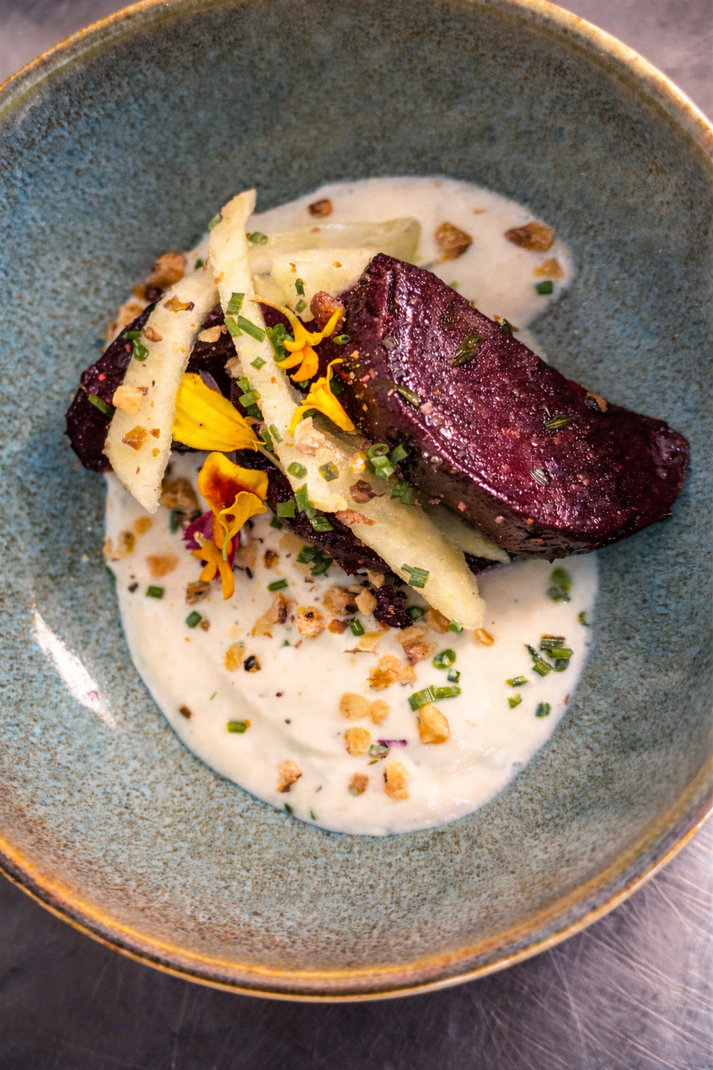 Plat gastronomique présenté dans un bol bleu, composé de viande saisie, de sauce crémeuse et de légumes.