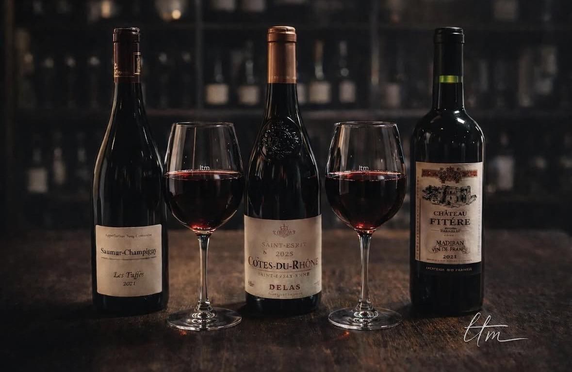 Trois bouteilles de vin et deux verres de vin rouge sur une table sombre dans un bar tamisé