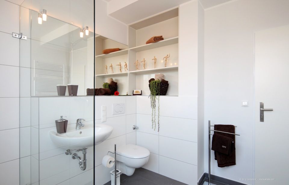 Weißes Badezimmer mit Waschbecken, Toilette und Regal mit Dekorationen. Dunkles Handtuch hängt am Gestell.