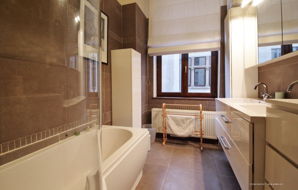 Modernes Badezimmer mit braunen Fliesen, weißen Schränken, Badewanne und Fenster.
