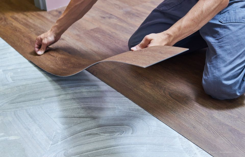 Person mit Handschuhen legt blaue Mosaikfliesen auf eine weiße Oberfläche, Kelle in der Nähe.