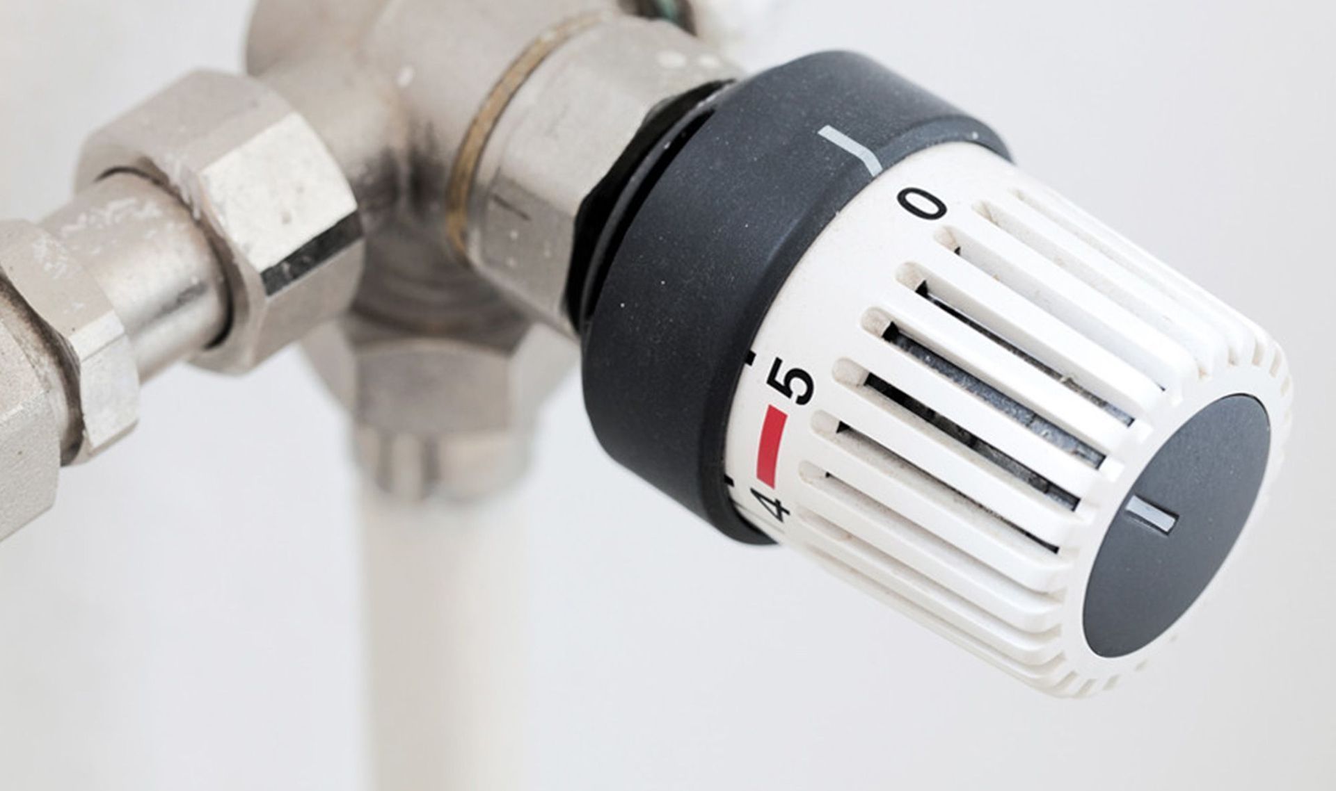Nahaufnahme eines weißen Heizkörperventils mit schwarzem Drehknopf, eingestellt auf 5.