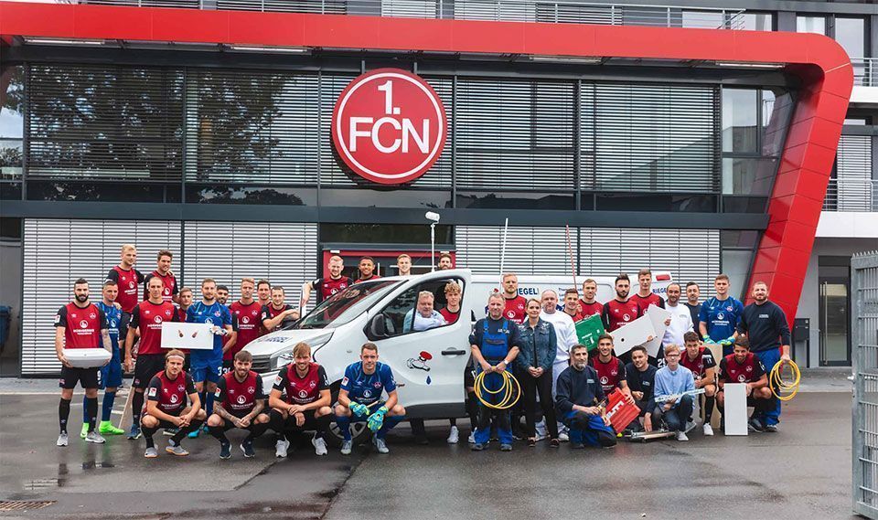 Eine Gruppe von Menschen posiert mit einem Rotkreuz-Transporter vor einem Gebäude mit dem Logo „1. FCN“.