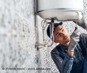 Klempner im karierten Hemd repariert mit einer Zange Waschbeckenrohre in einem Badezimmer.